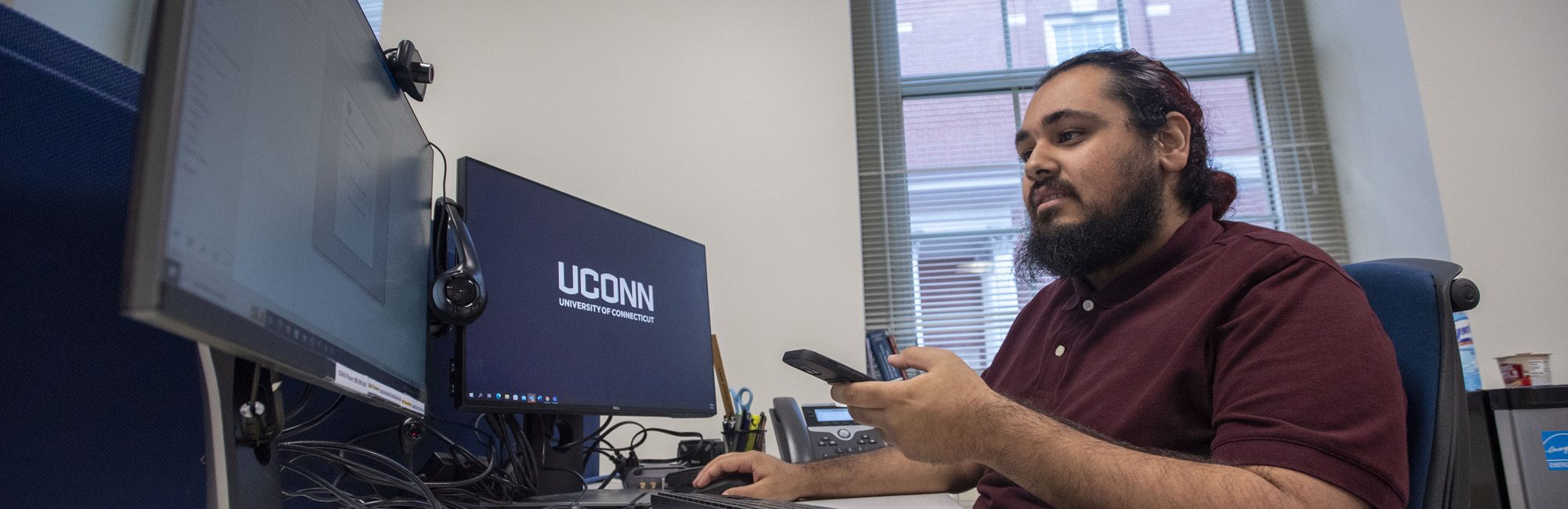 UConn Social Work student sitting in front of two large computer monitors.